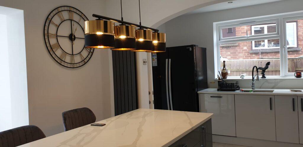 Maria's perfect kitchen view of the kitchen island with long gold lights above and clock in the background